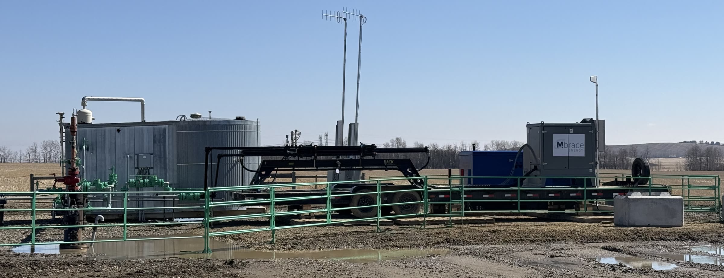 A producing well site: wellhead in the foreground, with the trailer-mounted Mbrace Field Unit and its power package set up beside the battery