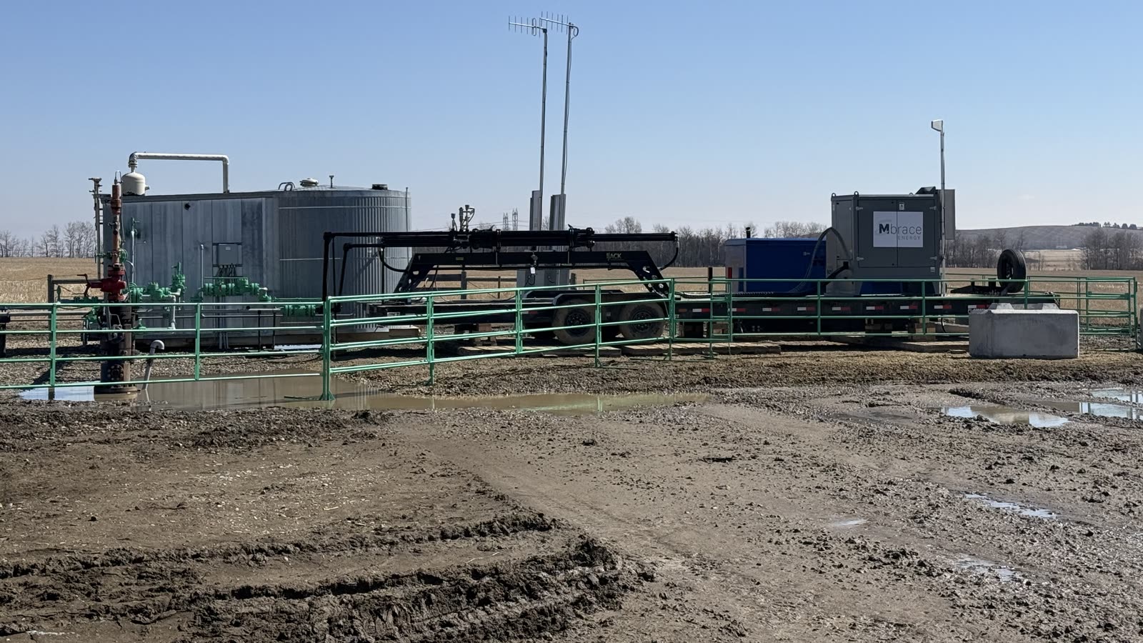 A producing well site with the wellhead in the foreground and the trailer-mounted Mbrace Field Unit and its power package set up beside the battery
