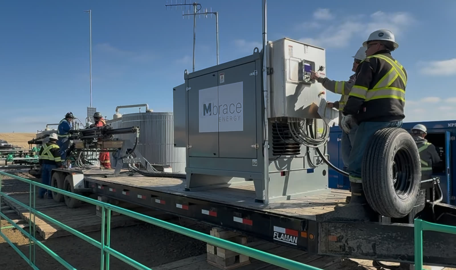An Mbrace Field Unit on a trailer at a well site, with two operators working at its control panel and a genset behind